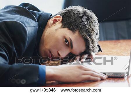 Portrait of a businessman resting his head on a desk in front of a laptop View Large Photo Image Stock Image - Portrait of a businessman resting his head on a desk in front of a laptop. Fotosearch
