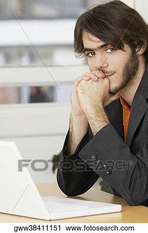 Portrait of a businessman sitting in front of a laptop at a table View Large Photo Image Stock Image - Portrait of a businessman sitting in front of a laptop at a table. Fotosearch