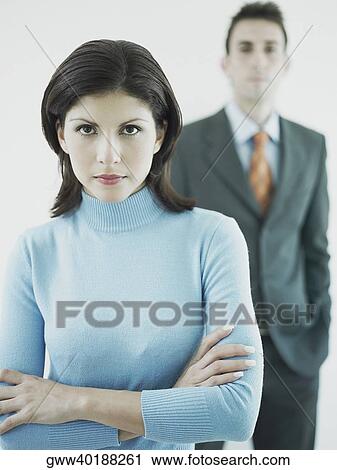 Portrait of a businesswoman standing with his arms crossed and a businessman standing behind her View Large Photo Image Stock Image - Portrait of a businesswoman standing with his arms crossed and a businessman standing behind her. Fotosearch