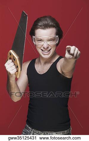 Stock Image - Portrait of a carpenter holding a saw and pointing forward. Fotosearch