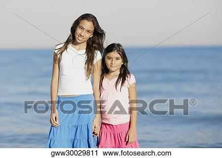 Portrait of a girl and her sister standing on the beach View Large Photo Image Stock Image - Portrait of a girl and her sister standing on the beach. Fotosearch