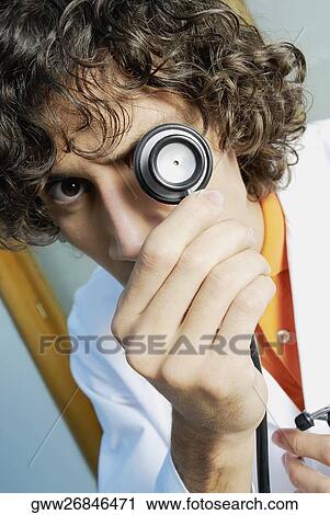Stock Image - Portrait of a male doctor covering his eye with a stethoscope. Fotosearch