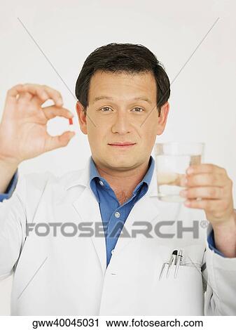 Portrait of a male doctor holding a glass of water and a capsule View Large Photo Image Stock Image - Portrait of a male doctor holding a glass of water and a capsule. Fotosearch
