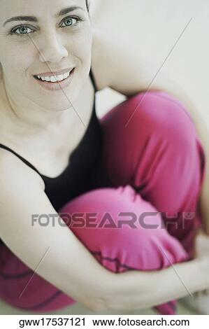 Stock Image - Portrait of a mature woman smiling and hugging her knees. Fotosearch