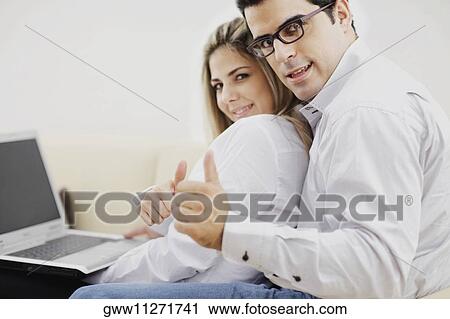 Portrait of a mid adult couple sitting in front of a laptop and showing thumbs up signs View Large Photo Image Stock Image - Portrait of a mid adult couple sitting in front of a laptop and showing thumbs up signs. Fotosearch