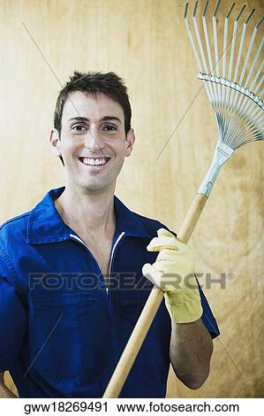 Stock Image - Portrait of a mid adult man holding a rake. Fotosearch