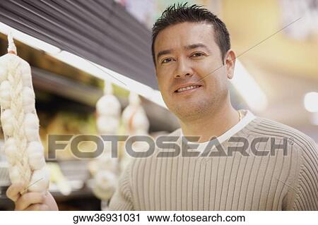 Portrait of a mid adult man holding hanged garlic in a vegetable market View Large Photo Image Stock Image - Portrait of a mid adult man holding hanged garlic in a vegetable market. Fotosearch