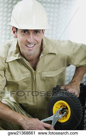 Stock Image - Portrait of a mid adult man tightening a nut of a wheel. Fotosearch