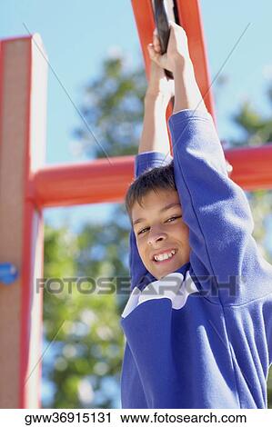 Stock Image - Portrait of a teenage boy hanging from a jungle gym. Fotosearch