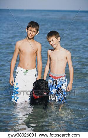 Portrait of a teenage boy standing with his brother and a dog in water View Large Photo Image Stock Image - Portrait of a teenage boy standing with his brother and a dog in water. Fotosearch