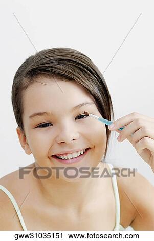 Stock Image - Portrait of a teenage girl applying eyeshadow on her eyes. Fotosearch