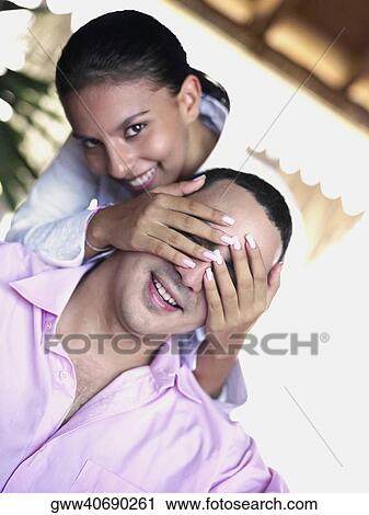 Stock Image - Portrait of a teenage girl covering a young man's eyes. Fotosearch