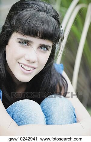 Stock Image - Portrait of a teenage girl hugging her knees and smiling. Fotosearch