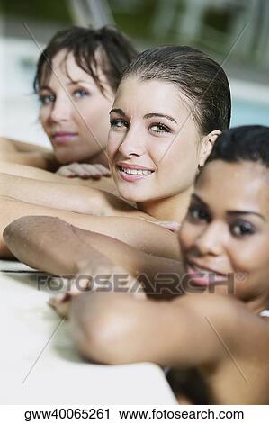 Stock Image - Portrait of a teenage girl with two young women leaning against the edge of a swimming pool. Fotosearch