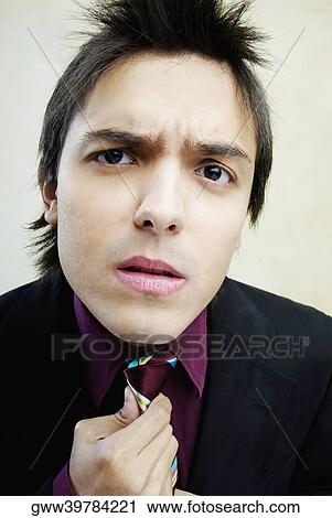Stock Image - Portrait of a young man adjusting his tie. Fotosearch
