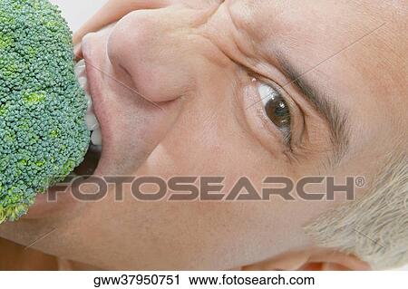 Stock Image - Portrait of a young man eating broccoli. Fotosearch