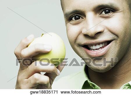 Stock Image - Portrait of a young man holding a green apple and smiling. Fotosearch
