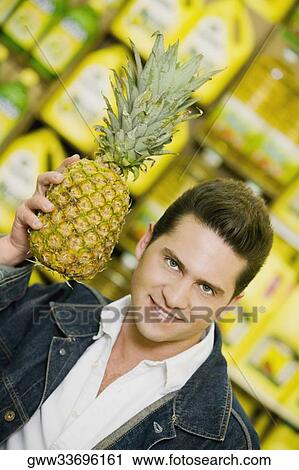 Portrait of a young man holding a pineapple in a supermarket View Large Photo Image Stock Image - Portrait of a young man holding a pineapple in a supermarket. Fotosearch