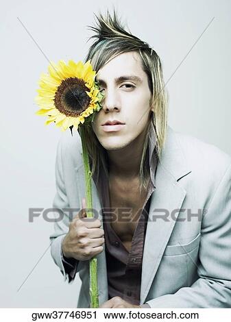 Stock Image - Portrait of a young man holding a sunflower in front of his eye (Helianthus Annuus). Fotosearch