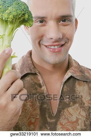 Stock Image - Portrait of a young man holding broccoli. Fotosearch