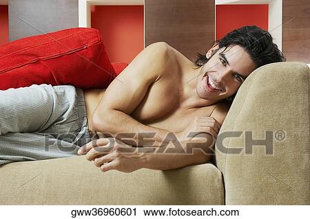 Stock Image - Portrait of a young man lying on a couch and smiling. Fotosearch