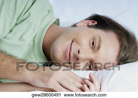Stock Image - Portrait of a young man lying on the bed and grinning. Fotosearch