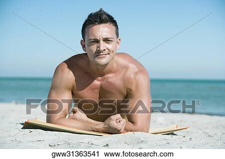 Stock Image - Portrait of a young man lying on the beach. Fotosearch
