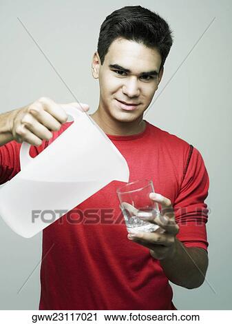 Stock Image - Portrait of a young man pouring water in a glass from a jug. Fotosearch