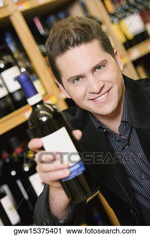Portrait of a young man showing a wine bottle in a liquor store View Large Photo Image Stock Image - Portrait of a young man showing a wine bottle in a liquor store. Fotosearch
