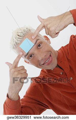 Stock Image - Portrait of a young man smiling with an adhesive note on his forehead. Fotosearch