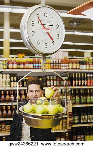 Portrait of a young man weighing apples on a weighing scale in a supermarket View Large Photo Image Stock Image - Portrait of a young man weighing apples on a weighing scale in a supermarket. Fotosearch