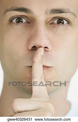 Stock Image - Portrait of a young man with his finger on his lips. Fotosearch