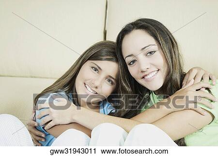 Stock Image - Portrait of a young woman and a teenage girl hugging each other and smiling. Fotosearch