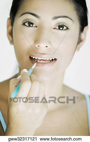 Portrait of a young woman applying lipstick on her lips with a make-up brush View Large Photo Image Stock Image - Portrait of a young woman applying lipstick on her lips with a make-up brush. Fotosearch