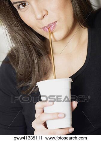 Stock Image - Portrait of a young woman drinking a cold drink with a drinking straw. Fotosearch