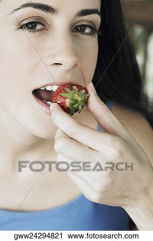 Stock Image - Portrait of a young woman eating a strawberry. Fotosearch