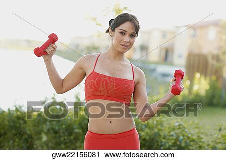Stock Image - Portrait of a young woman exercising with dumbbells. Fotosearch