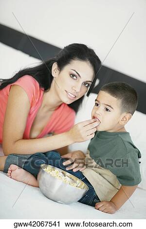 Stock Image - Portrait of a young woman feeding popcorn to her son. Fotosearch