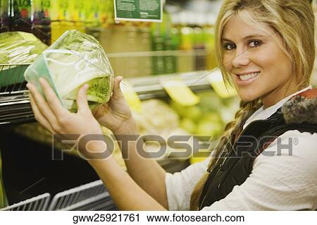 Stock Image - Portrait of a young woman holding a cabbage in a supermarket. Fotosearch
