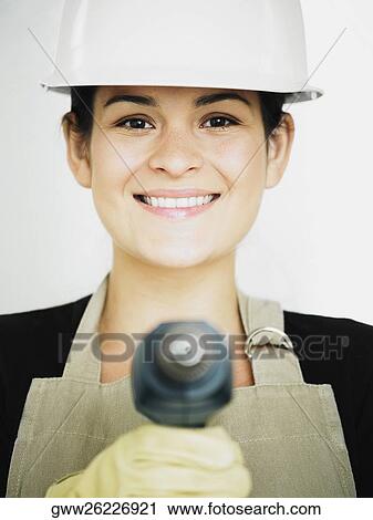 Stock Image - Portrait of a young woman holding a drill and smiling. Fotosearch