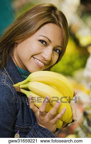 Portrait of a young woman holding a bunch of bananas and smiling View Large Photo Image Stock Image - Portrait of a young woman holding a bunch of bananas and smiling. Fotosearch