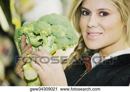Stock Image - Portrait of a young woman holding a broccoli. Fotosearch