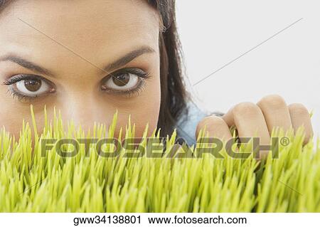 Stock Image - Portrait of a young woman peeking over wheatgrass. Fotosearch