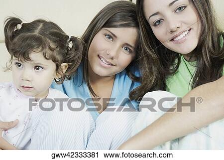 Portrait of a young woman sitting and her two sisters smiling View Large Photo Image Stock Image - Portrait of a young woman sitting and her two sisters smiling. Fotosearch