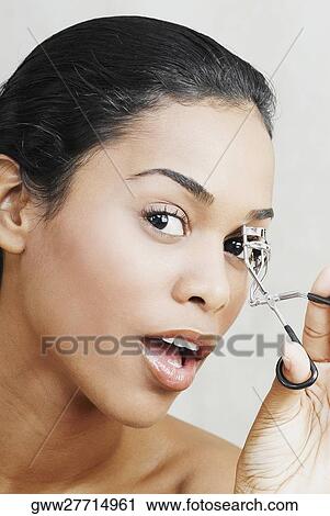 Stock Image - Portrait of a young woman using a eyelash curler. Fotosearch