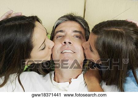 Stock Image - Portrait of mature man being kissed by his two daughters. Fotosearch