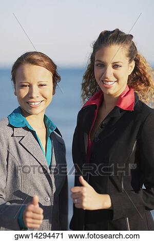 Stock Image - Portrait of two young women showing thumbs up signs. Fotosearch