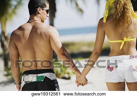 Rear view of a couple holding hands View Large Photo Image Stock Image - Rear view of a couple holding hands. Fotosearch