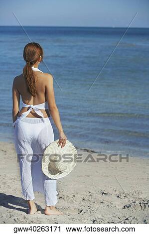 Rear view of a woman standing on the beach and holding a straw hat View Large Photo Image Stock Image - Rear view of a woman standing on the beach and holding a straw hat. Fotosearch