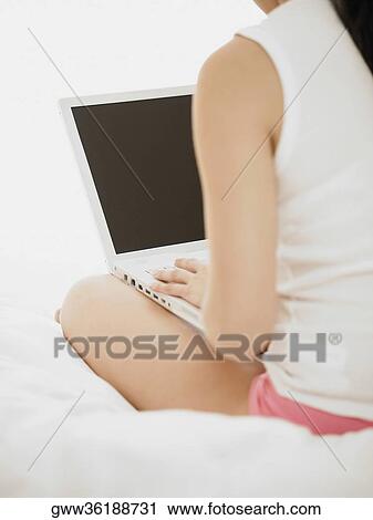 Rear view of a woman using a laptop on the bed View Large Photo Image Stock Image - Rear view of a woman using a laptop on the bed. Fotosearch